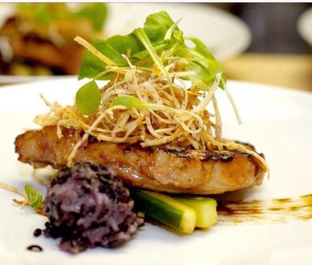 A plated fish course with black rice and crispy shallots