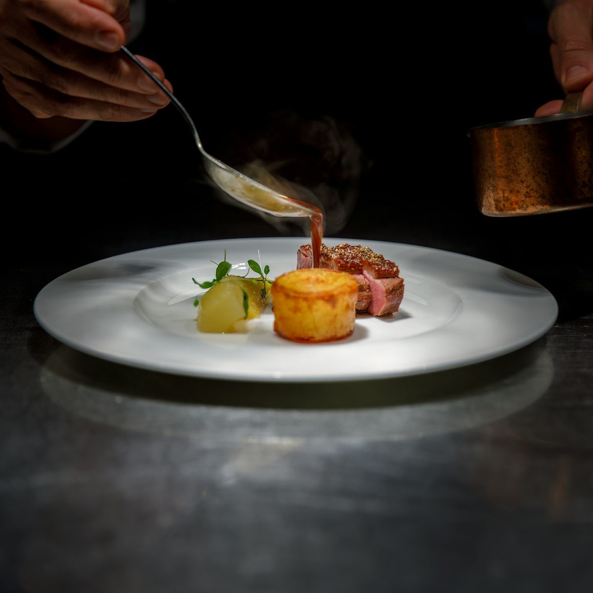 A chef saucing a plated dish in low light